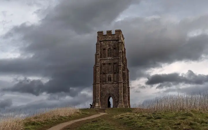 Glastonbury Tor with the roofless tower of St Michael's Church on its summit under a grey sky