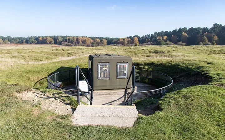 The grassy, cratered landscape of Grime's Graves flint mines in Breckland, with a shaft entrance building