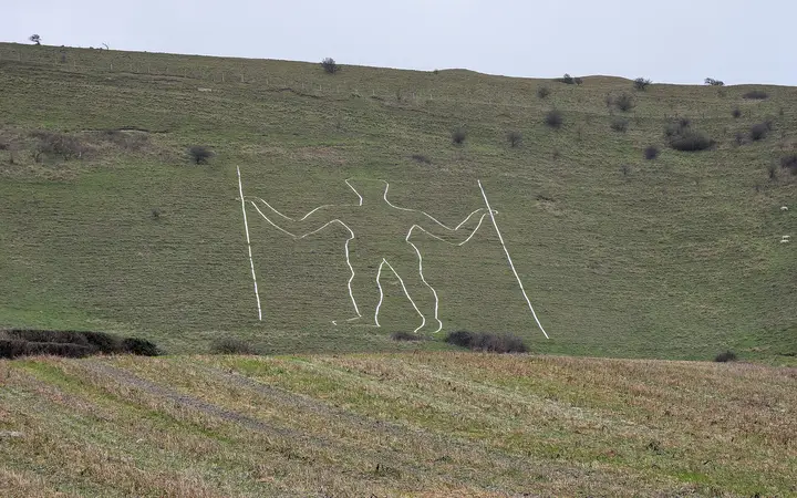 The tall outline figure of the Long Man of Wilmington on a green South Downs slope