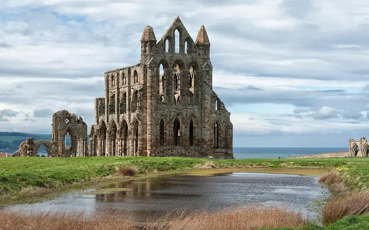 The ruined Gothic east end of Whitby Abbey reflected in a pond on the clifftop